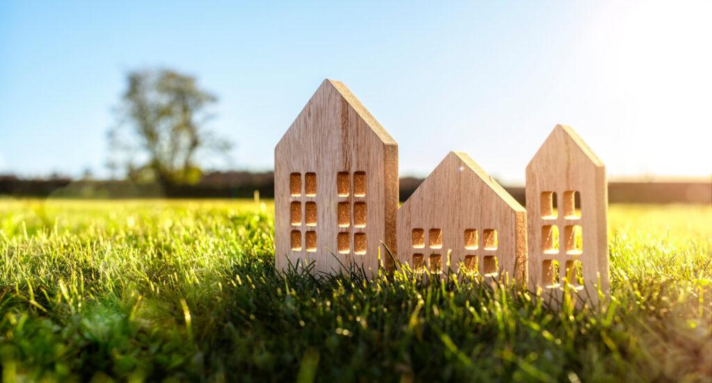 Holzmodellhaus auf leerem Feld bei Sonnenuntergang, Konzept für Bau und Immobilien.